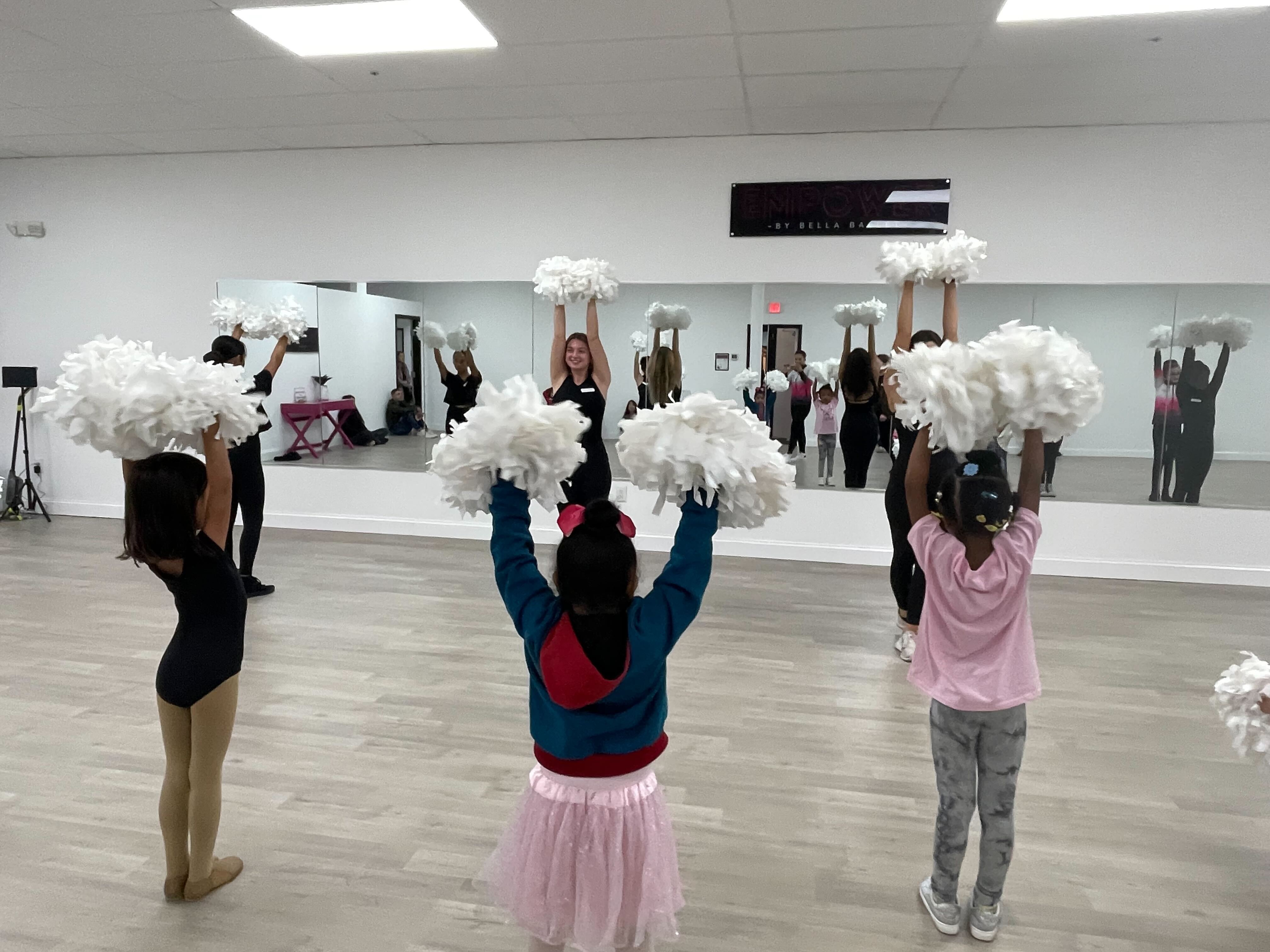 Children raising pom-poms with their instructor during a dance class